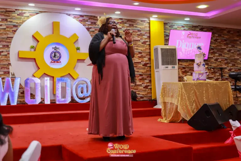 A speaker in a rose-coloured dress addresses the guests in front of the WOID@5 letters.